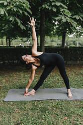 Fitness instructor practicing triangle pose yoga in park - MRRF02470