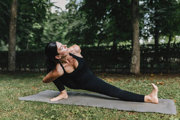 Fitness instructor exercising Skandasana pose in park - MRRF02471