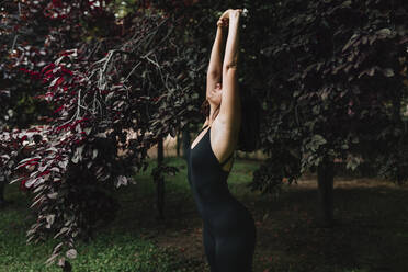 Yoga teacher practicing Urdhva Hastasana pose in park at sunset - MRRF02474