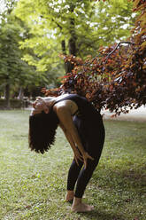 Yogalehrer bei Dehnungsübungen auf Gras im Park - MRRF02475