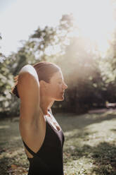 Yoga instructor with eyes closed enjoying sunlight in park - MRRF02477