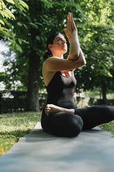 Yoga teacher exercising vajrasana garudasana posture in park - MRRF02485