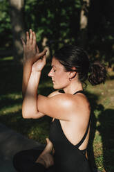 Yoga teacher with eyes closed exercising vajrasana garudasana posture in park - MRRF02486