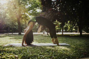 Yoga instructor practicing bridge pose in park - MRRF02490