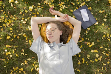 Young woman lying down with eyes closed in autumn park - LESF00318