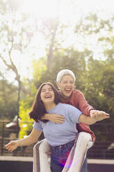 Cheerful woman giving piggyback ride to friend on sunny day - EGCF00056