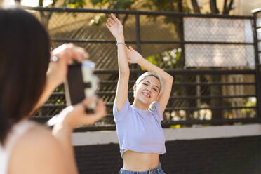 Woman photographing friend through camera on sunny day - EGCF00062