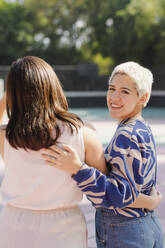 Happy non-binary person with friend standing on sunny day - EGCF00066