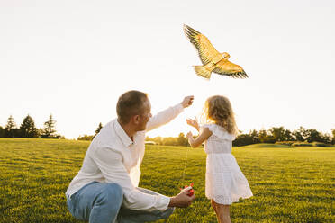 Father teaching daughter to fly kite at sunset - SIF00497