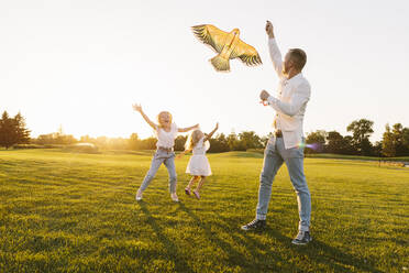 Father and daughter enjoying flying kite in park at sunset - SIF00498