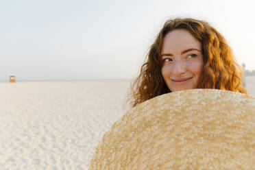 Smiling woman with oversized straw hat at beach - TYF00433