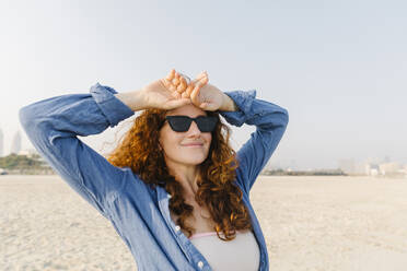 Smiling woman wearing sunglasses at beach - TYF00434