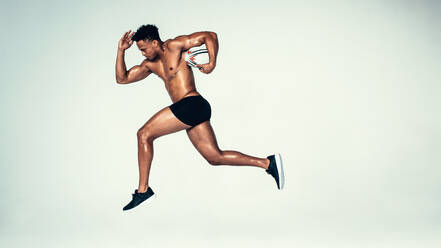 Side view shot of young man training with rugby ball. Male model with muscular build running with rugby ball over grey background. - JLPSF00006