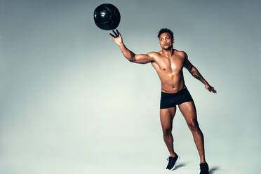 Aufnahme eines fitten jungen Mannes, der mit einem Medizinball trainiert. Afrikanischer Mann trainiert mit einem Medizinball auf grauem Hintergrund. - JLPSF00010