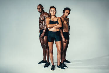 Full length portrait of young men and woman with muscular body standing together over grey background. Group of muscular people looking at camera. - JLPSF00020