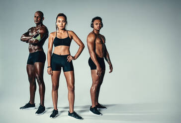 Full length portrait of healthy young men and woman with muscular build standing together over grey background. Group of muscular people looking at camera. - JLPSF00022