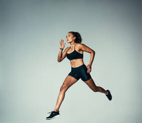 Voller Länge Schuss von hispanischen weiblichen Athleten tun laufen Übung über grauen Hintergrund. Fitness Frau läuft. - JLPSF00036
