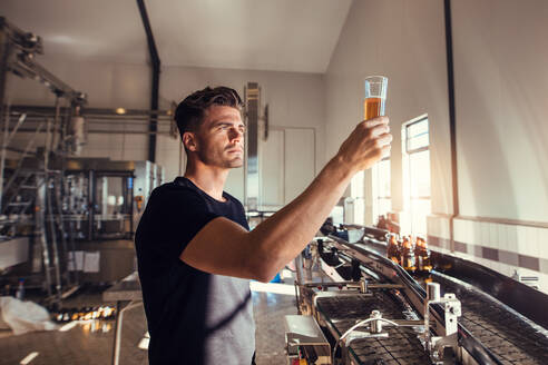 Junger Mann, der in einer Brauerei die Qualität von Craft Beer prüft. Männlicher Inspektor, der in einer Fabrik zur Herstellung von Alkohol arbeitet und das Bier kontrolliert. - JLPSF00058