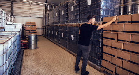 Junger Geschäftsmann betrachtet die verpackten Bierkästen im Lager. Brauereibesitzer überprüft die Bierkästen im Auslieferungslager. - JLPSF00111