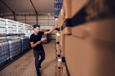 Junger Mann bei der Bestandsaufnahme von verpacktem Bier in einem Lagerhaus. Lagerleiter bei der Bestandsaufnahme von Fertigwaren in einer Brauerei. - JLPSF00112