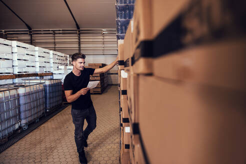 Young man taking the stock of packaged beer boxed in warehouse. Warehouse manager taking finished goods inventory at brewery. - JLPSF00112