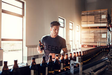 Junger Mann arbeitet in einer kleinen Bierfabrik und prüft die Qualität des Biers. Junger Geschäftsmann prüft die Bierflasche in einer Brauerei. - JLPSF00117