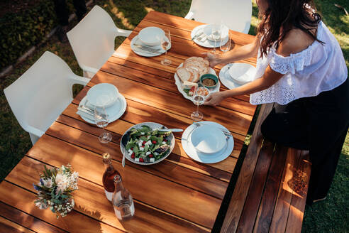 Draufsicht auf eine Frau, die Essen auf einen Holztisch für eine Einweihungsparty stellt. Eine Frau bereitet einen Tisch im Freien mit Essen und Trinken vor. - JLPSF00125