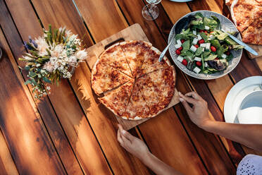 Top view of woman setting pizza and salad on wooden table for housewarming party. Female preparing a dining table outdoors with food for dinner. - JLPSF00128