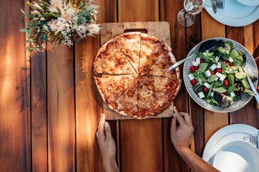 Top view of female hands setting food on the table for a party. Woman setting pizza and salad on wooden table for housewarming party. - JLPSF00129