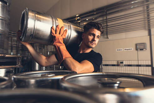 Shot of brewer carrying keg at brewery factory. Young man with metal beer barrels at warehouse. - JLPSF00135