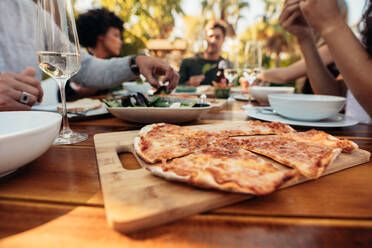 Delicious pizza on wooden table with people eating food. Friends having party outdoors. - JLPSF00139