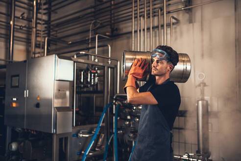 Shot of young man with metal beer barrels at brewery. Brewer carrying keg at brewery plant. - JLPSF00156