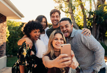 Group of people partying together and taking selfie. Young friends at housewarming party taking selfie with smart phone. - JLPSF00164