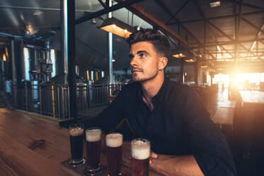 Young man tasting different types of beer at the brewery factory. Four different varieties of craft beer on a wooden table - JLPSF00176