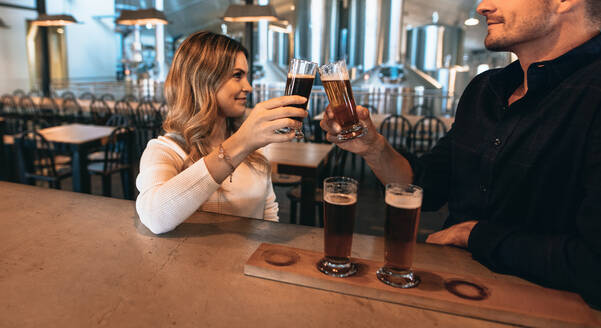 Ein Paar an der Bar mit verschiedenen Sorten Craft-Bier. Sie sind in einer Brauerei und stoßen mit Biergläsern an. - JLPSF00179