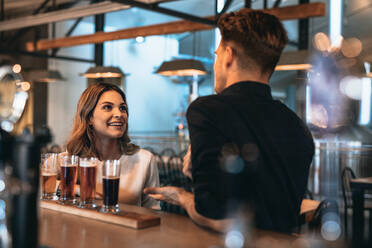 Junges Paar an der Bar mit verschiedenen Craft-Bieren auf einem Holztisch. Mann und Frau unterhalten sich an der Theke. - JLPSF00183
