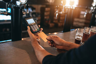 Beschnittenes Bild eines Mannes, der mit einer Kreditkarte an einer Bar bezahlt. Ein Mann in einer Brauerei mit verschiedenen Biersorten auf dem Tresen. - JLPSF00185