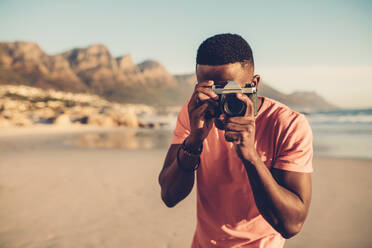 Schwarzer Mann mit Digitalkamera am Strand. Afroamerikanischer Mann fotografiert am Meer. - JLPSF00195