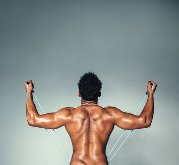 Rear view square shot of fitness male model using stretch band. Young man exercising with elastic band on grey background. - JLPSF00200