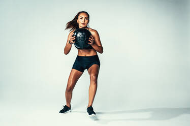 Studio shot of fit young woman with medicine ball. Female model with muscular body exercising with fitness ball over grey background. - JLPSF00205