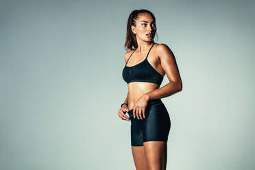 Porträt einer Fitness-Frau in Sportkleidung, die vor einem grauen Hintergrund steht und wegschaut. Hispanisches weibliches Modell im Studio. - JLPSF00211