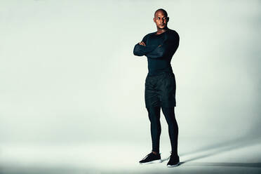 Full length portrait of fitness men in sportswear with his arms crossed. Male bodybuilder standing over grey background and looking away. - JLPSF00231