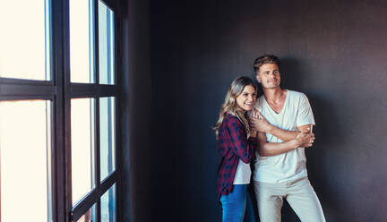 Portrait of beautiful young couple standing together indoors. Smiling young woman with her boyfriend looking away. - JLPSF00241