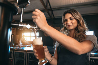 Junge Frau zapft Bier in einer Bar aus Metallzapfhähnen. Schöne Barkeeperin zapft Bier in einer Bar. - JLPSF00243