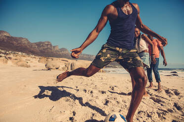 Eine Gruppe von Freunden spielt Fußball am Strand. Junge Leute spielen in den Sommerferien ein Fußballspiel am Meeresufer. - JLPSF00245