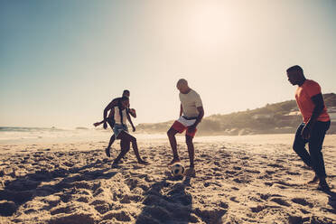 Eine Gruppe von Freunden hat Spaß am Strand und spielt Fußball. Junge Leute spielen Fußball am Sandstrand. - JLPSF00247