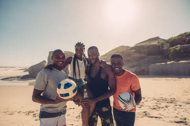Junge Freunde stehen zusammen am Strand mit American Football und Fußball. Gruppe von Freunden im Sommerstrandurlaub. - JLPSF00249
