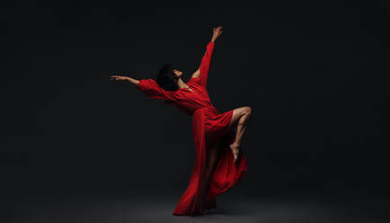 Female dancer performing contemporary dance style on black background. Woman in red dress dancing in studio. - JLPSF00253