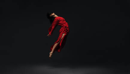 Zeitgenössische Tänzerin tanzt auf schwarzem Studiohintergrund. Tänzerin in rotem Seidenkleid tanzt barfuß im Studio. - JLPSF00254
