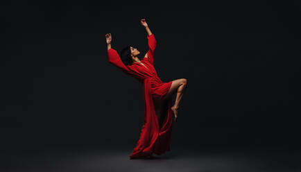 Full length of a young woman dancing in studio. Contemporary female dancer in red dress performing over black background. - JLPSF00265